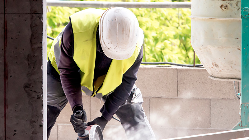 Construction worker wearing a safety helmet and high-visibility jacket with power tools on a construction site