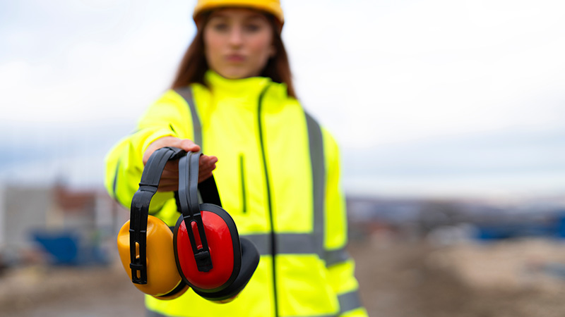 Werkvrouw in fluojas biedt gehoorbescherming aan