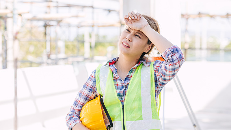 Une femme sur son lieu de travail, visiblement épuisée par la chaleur, le visage en sueur et l'attitude fatiguée