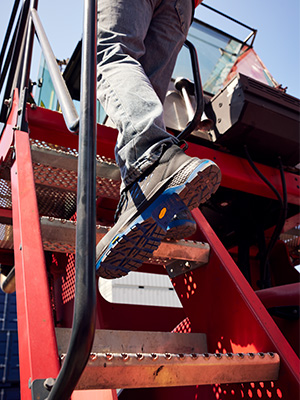 A worker climbs onto a bulldozer wearing EMMA Safety safety boots, as an example of safe footwear in a demanding work environment