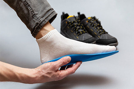 A man demonstrates how he holds an arch support against his foot, with safety boots in the background