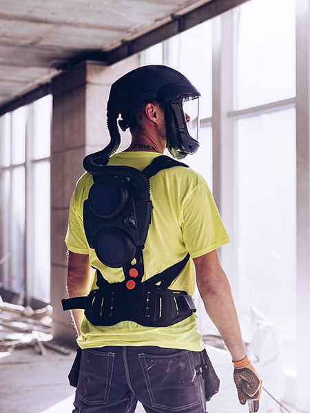 A construction site worker wearing a dust mask and Sundström respiratory protection on his back